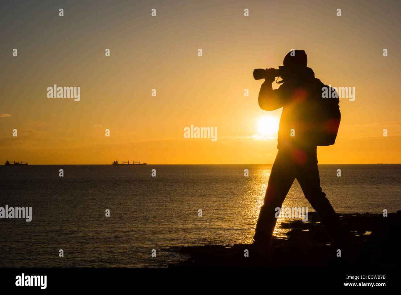 Tynemouth, North Tyneside, England, UK. Tuesday, 3rd March 2015. Weather: photographer at sunrise  on rocky outcrop near Tynemouth on a clear chilly morning on the north east coast. Credit:  ALANDAWSONPHOTOGRAPHY/Alamy Live News Stock Photo