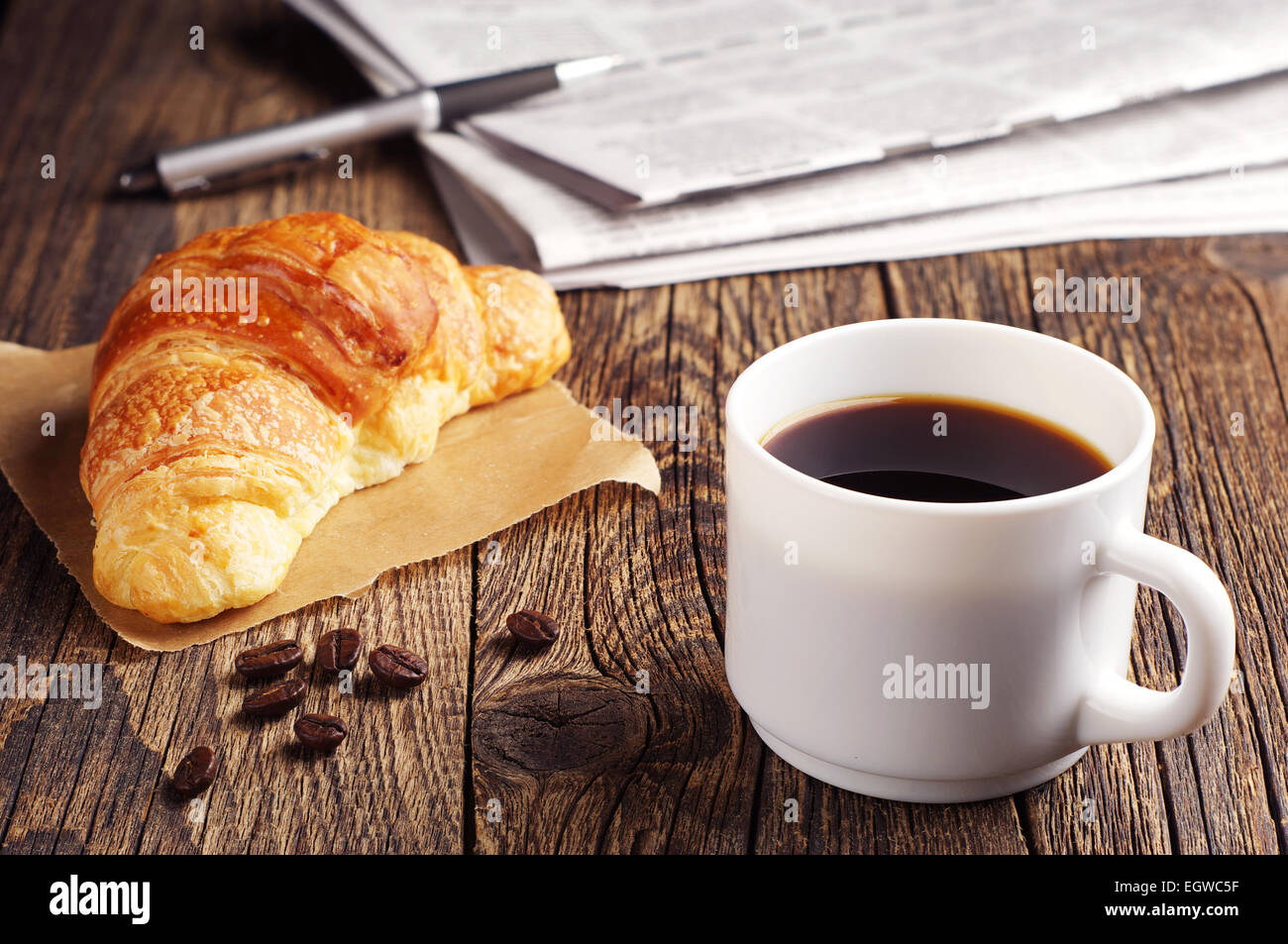 Cup of coffee, croissant and newspaper on wooden table Stock Photo