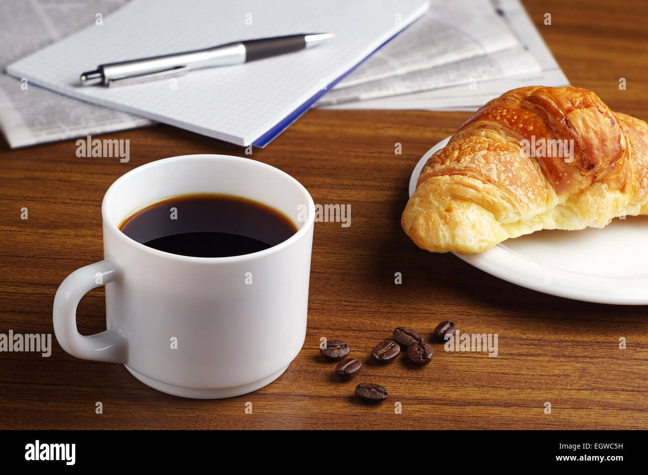 Cup of coffee, croissant, newspaper and notepad on wooden table Stock Photo