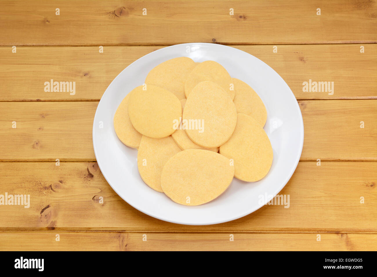 Pile of egg-shaped biscuits for Easter on a white plate on a wooden table Stock Photo