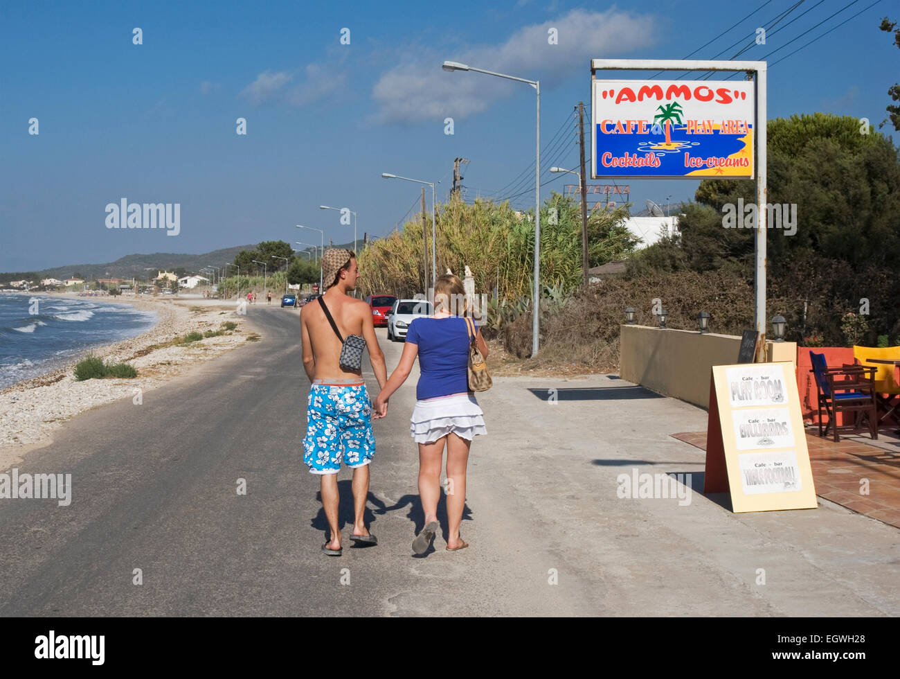 couple of young tourists walking along the seafront of Roda, Corfu Island, Greece Stock Photo