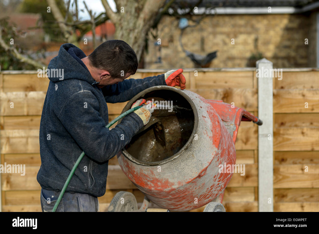 A labourer laborer hosing down the inside of a portable mortar concrete cement mixer on a home improvement project in Britain. Stock Photo