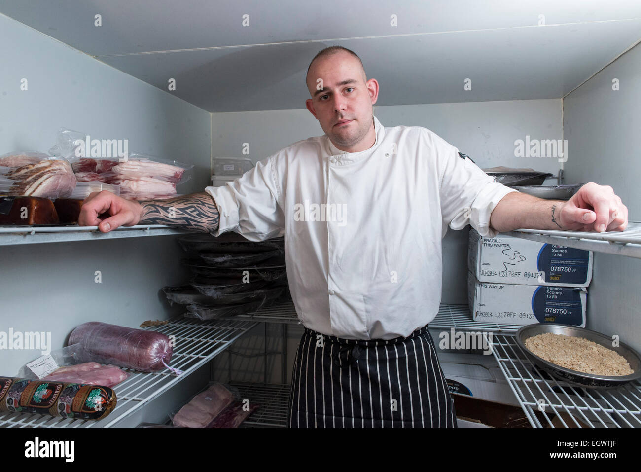 A professional mean ^ moody looking chef stands in his kitchen, looking annoyed with lots of cooking equipment in the background Stock Photo