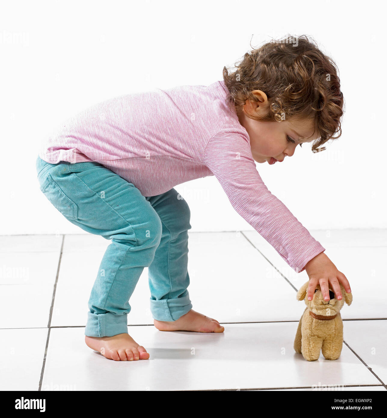 Young girl bending over to pick up soft toy dog, 2 years Stock Photo