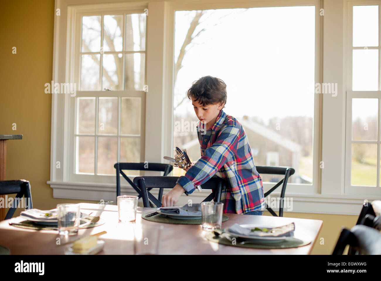 A young boy setting the table with cutlery and glasses. Stock Photo