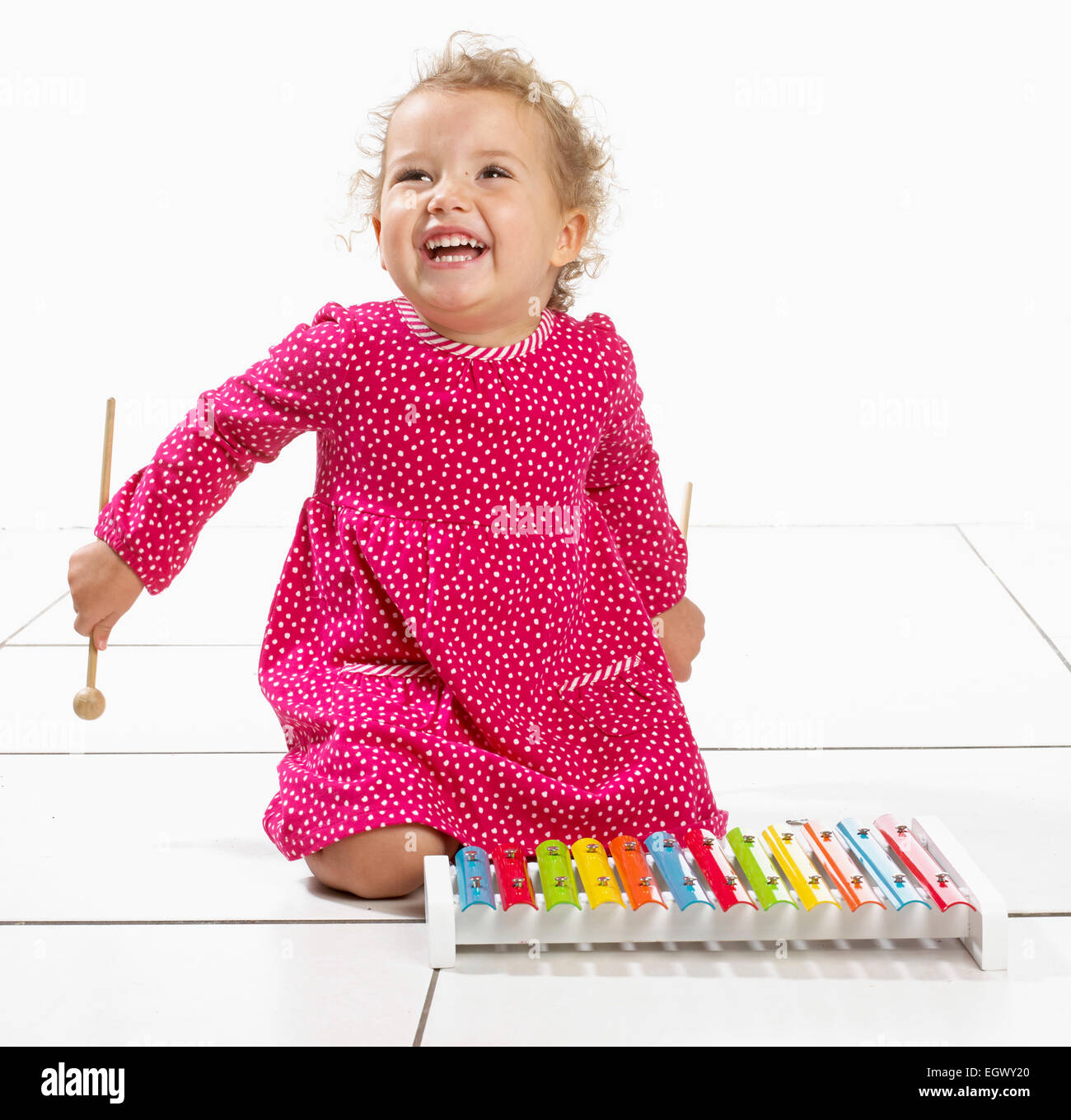 Small girl (2 years) kneeling on floor next to xylophone Stock Photo