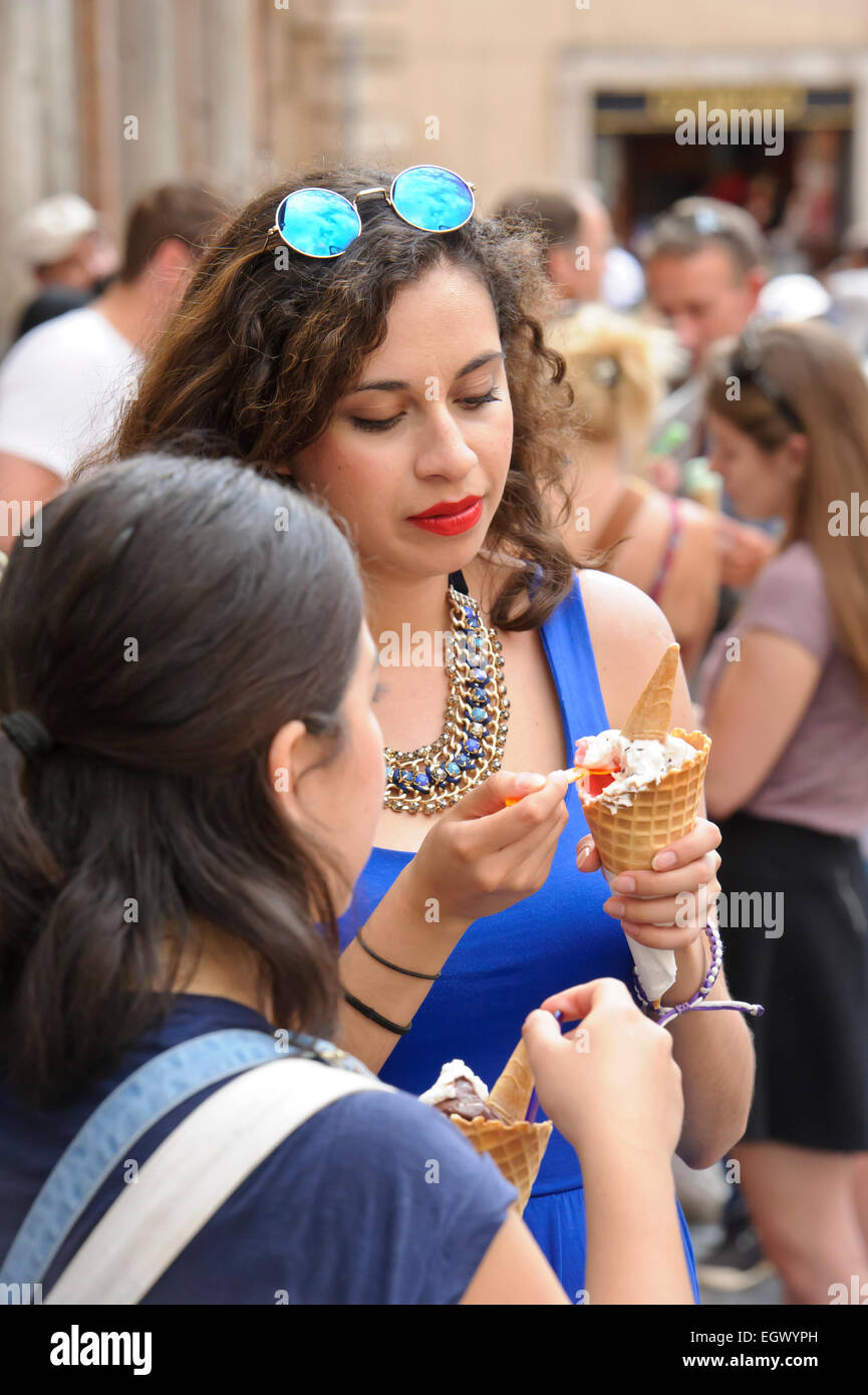 A young woman wearing a deep blue dress eating ice cream among the crowd on the street, Rome, Italy. Stock Photo