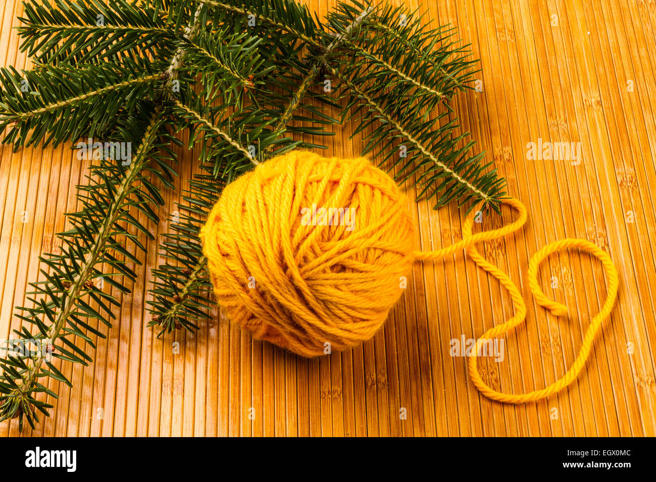 roll of yellow soft knitting yarn and yew branch on wooden background Stock Photo