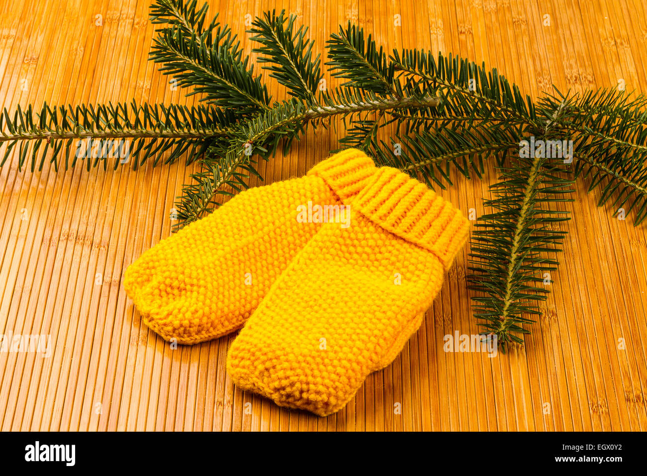 yellow soft knitting mittens and yew branch on wooden background Stock Photo