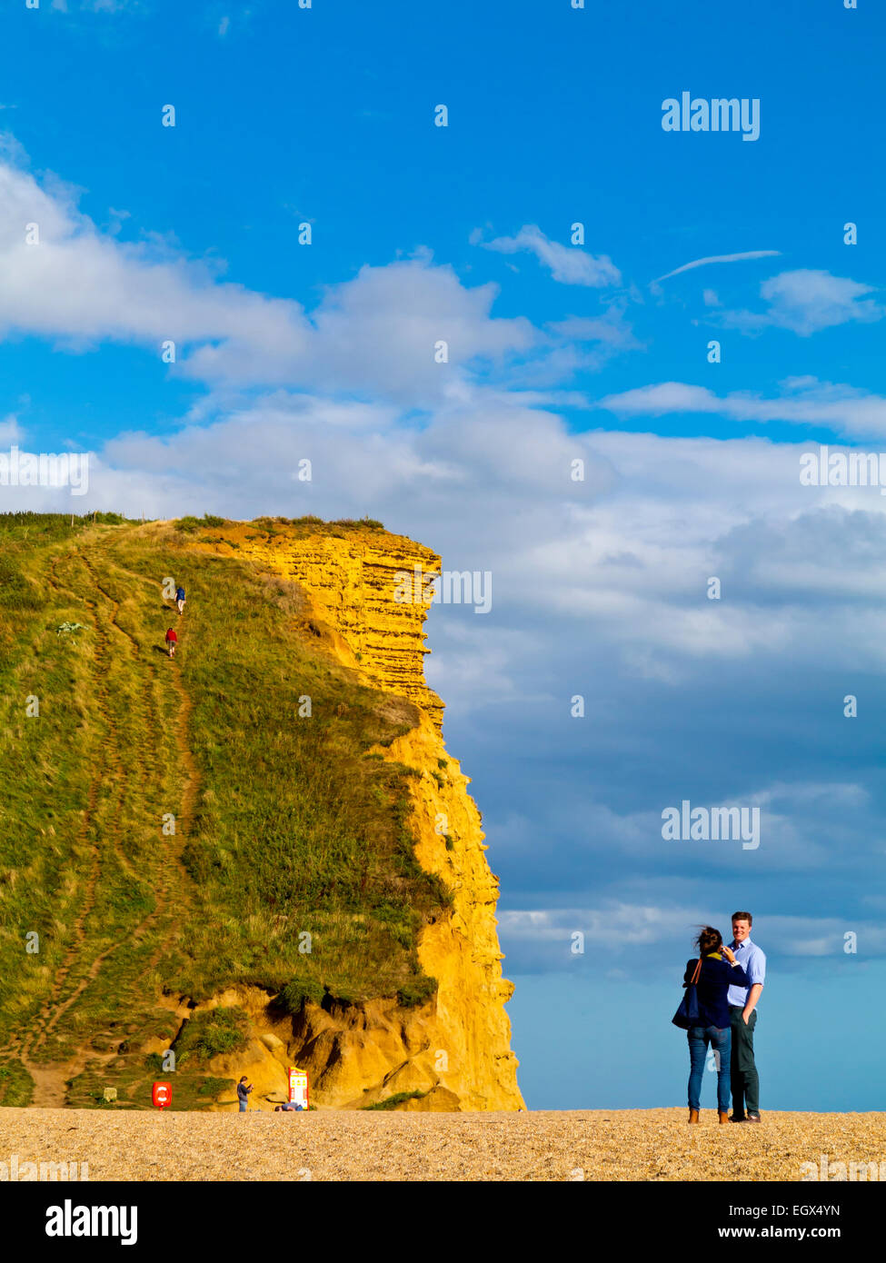 Couple standing next to dramatic sandstone cliffs and beach at West Bay on the Jurassic Coast in Dorset south west England UK Stock Photo