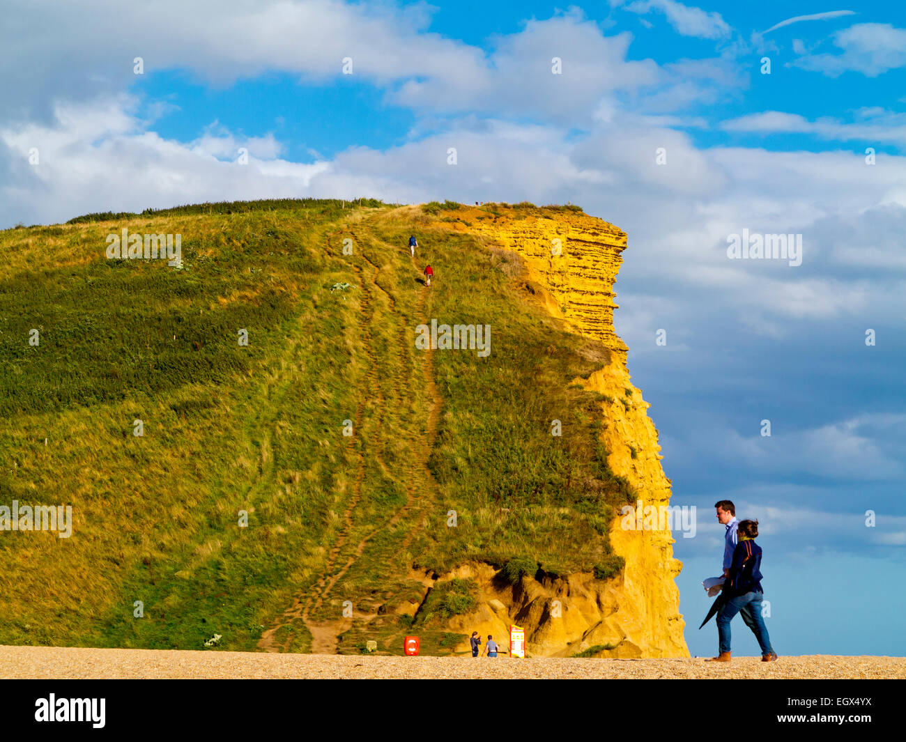 Couple standing next to dramatic sandstone cliffs and beach at West Bay on the Jurassic Coast in Dorset south west England UK Stock Photo