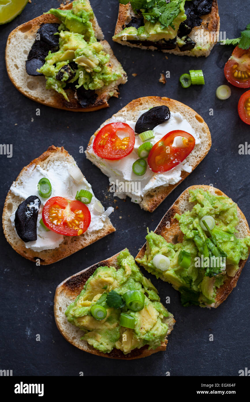 Canapes with avocado spread, goat cheese and black garlic Stock Photo