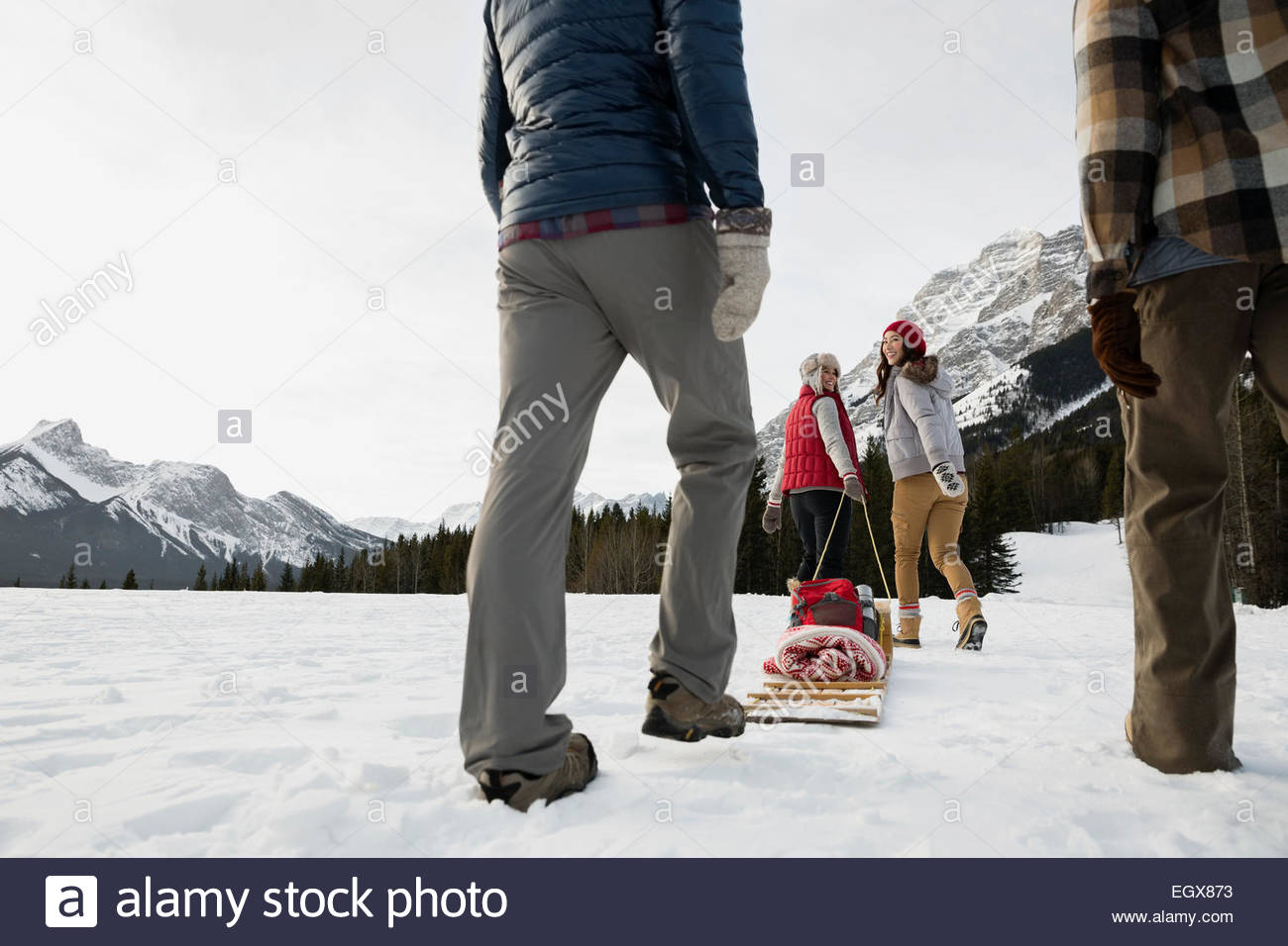 Couples sledding in snowy field below mountains Stock Photo