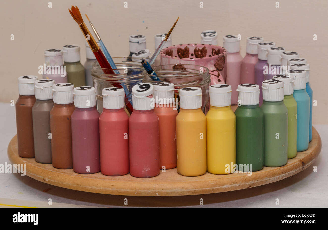Jars of ceramic  paint in many colours on a wooden spinners.  Brushes and water jars in the centre. Stock Photo