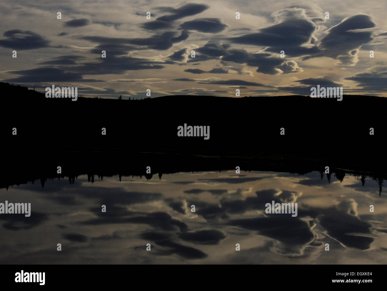 A cloud bedecked sky reflects into the still waters of a kettle hole