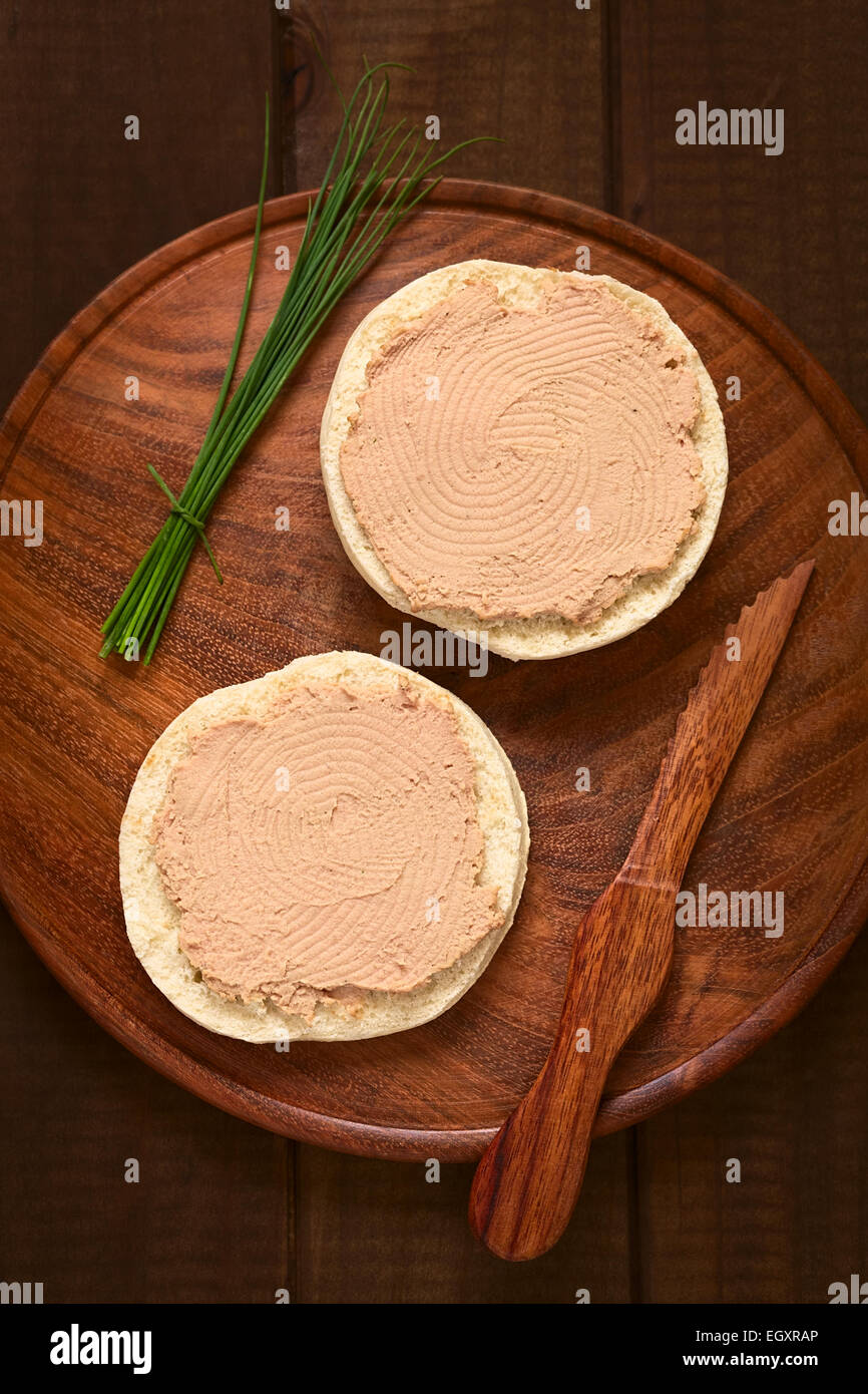 Overhead shot of liverwurst spread on bun with chives and knife on ...
