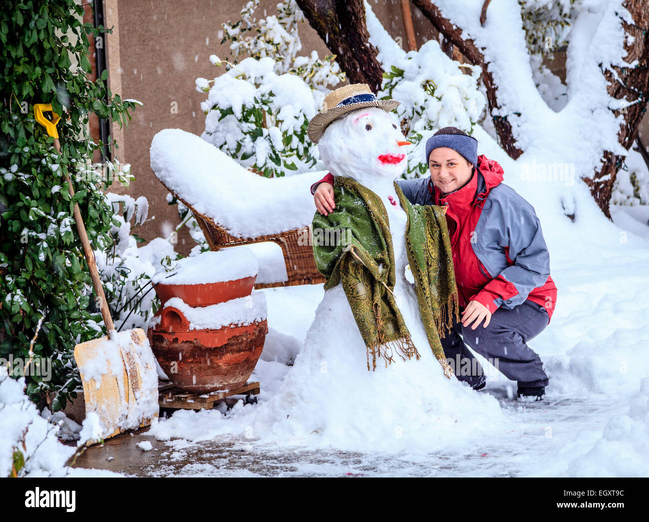 Woman is posing with a snowman in her front yard during snow storm