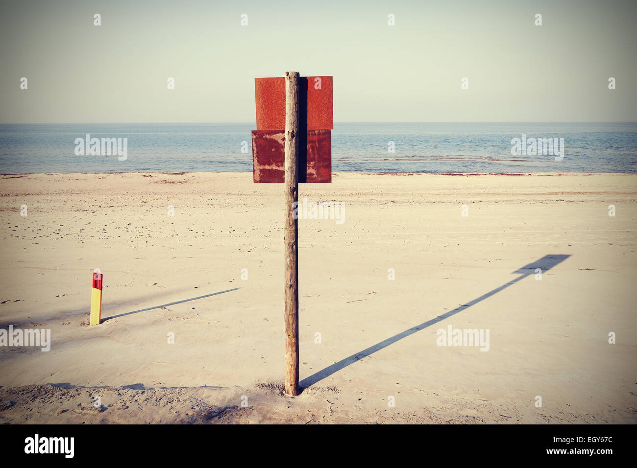 Retro filtered rusty board sign on wooden post on a beach. Stock Photo