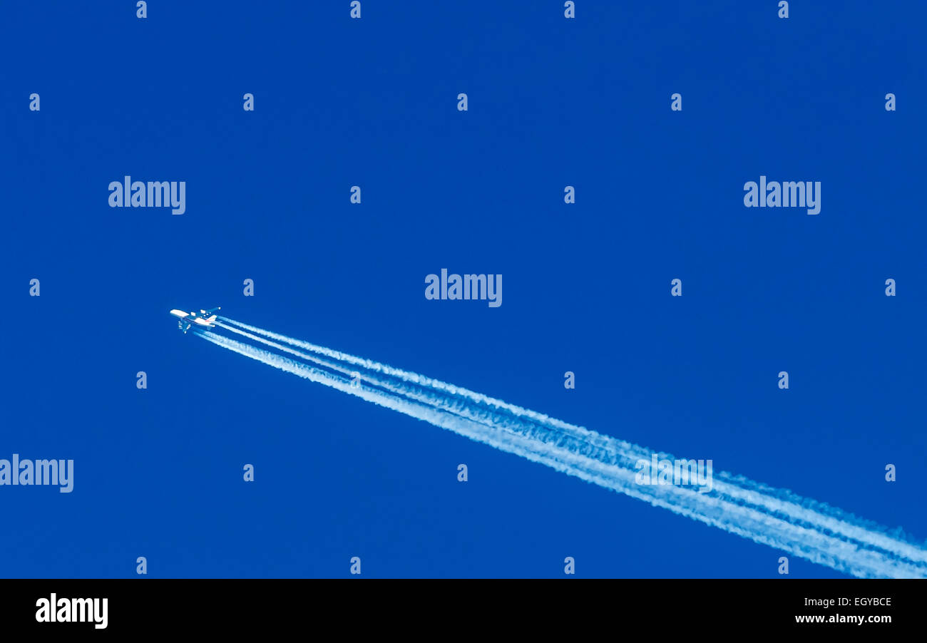 Flying airplane and vapour trail in front of blue sky Stock Photo