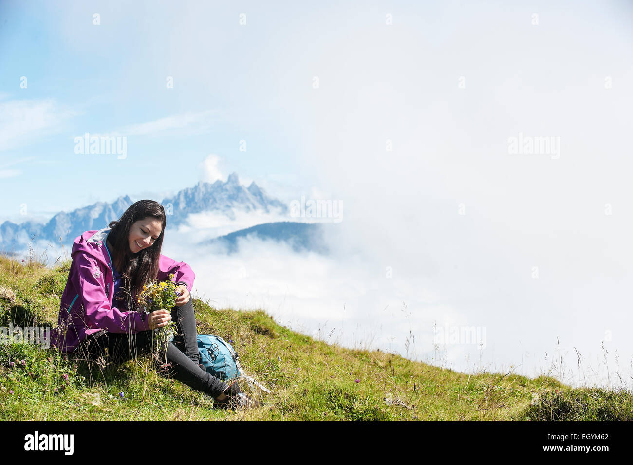Austria, Altenmarkt-Zauchensee, young woman sitting on alpine meadow Stock Photo