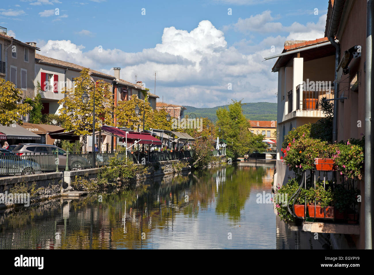 Town life goes on along the banks of the Sorgue River in the Vaucluse district of Southern France.  A shopping hub for antique., Stock Photo