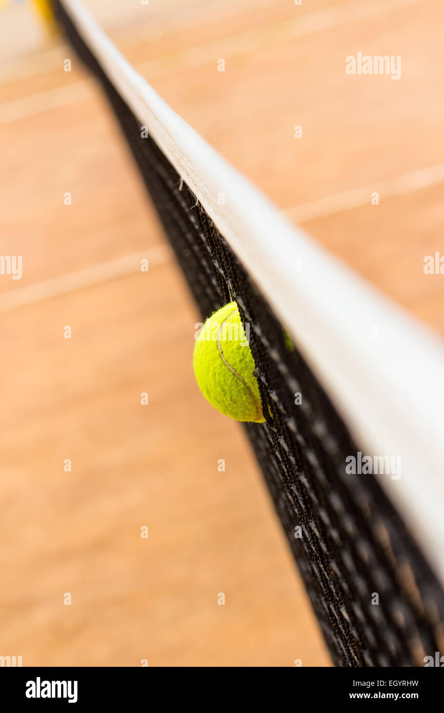 Yellowgreen tennis ball stuck in the grid on red clay courts. Small