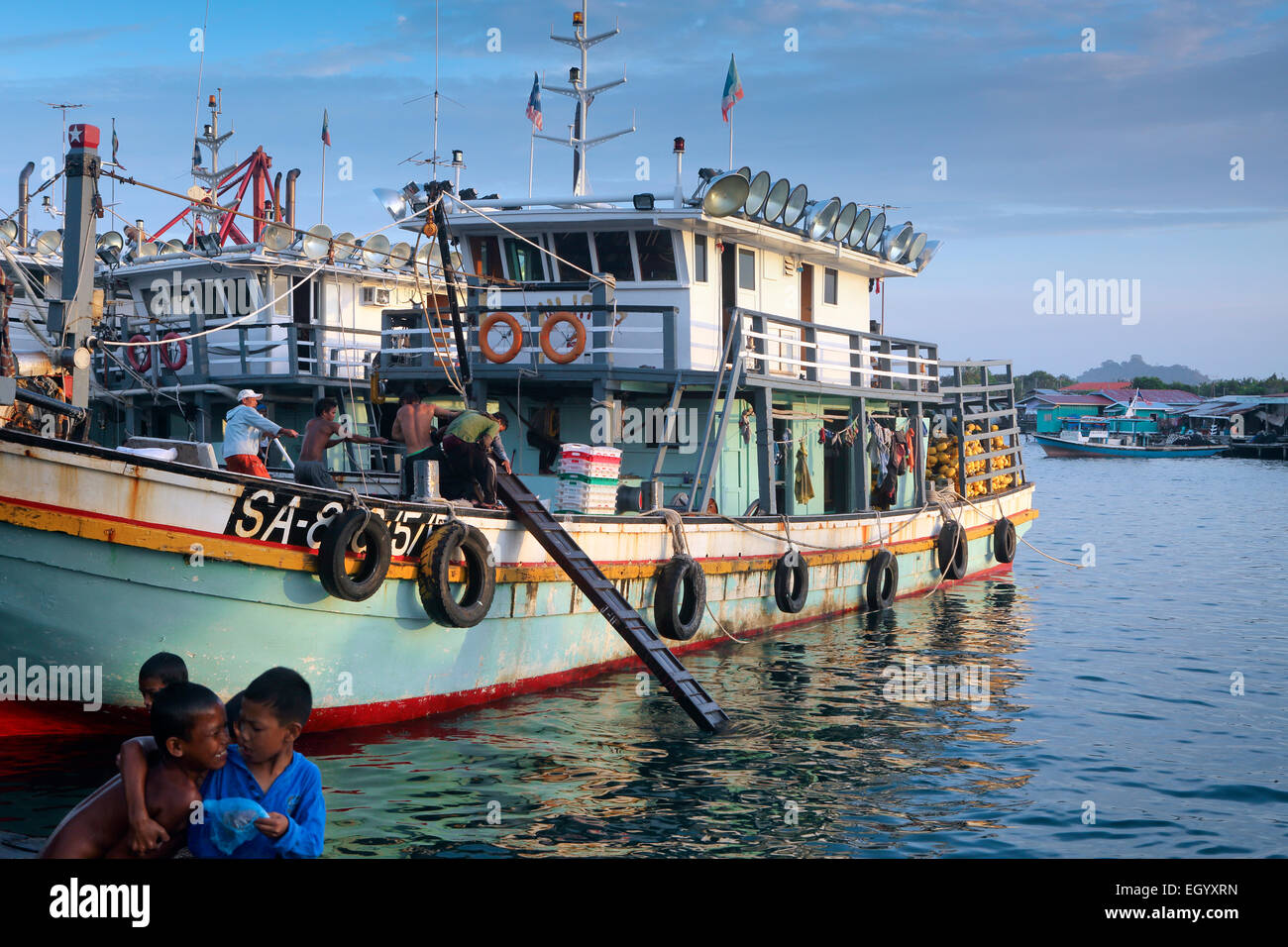 Children play as fishermen haul a ladder into a fishing boat at Semporna, Borneo Stock Photo