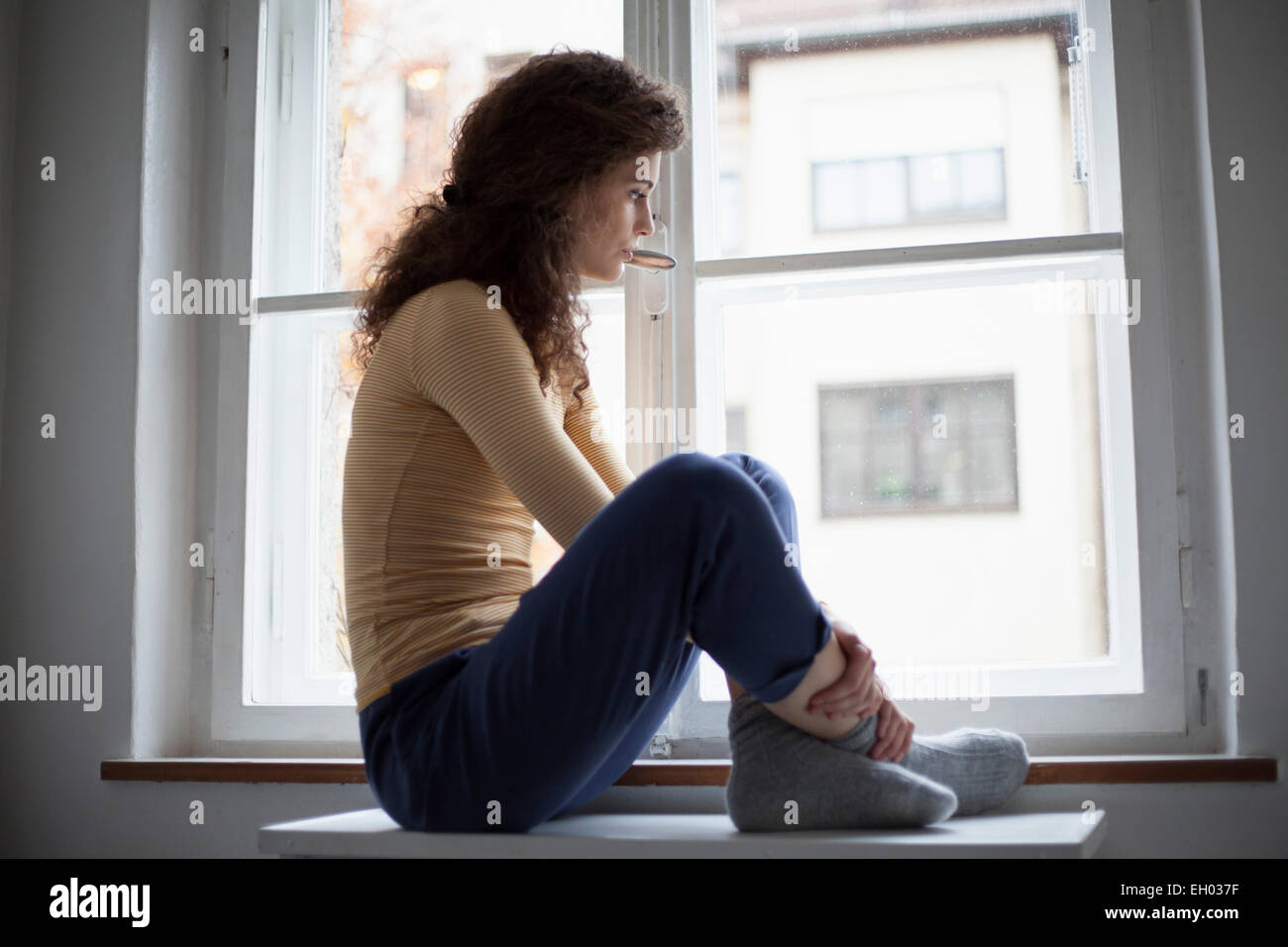 Sad young woman looking out of window Stock Photo