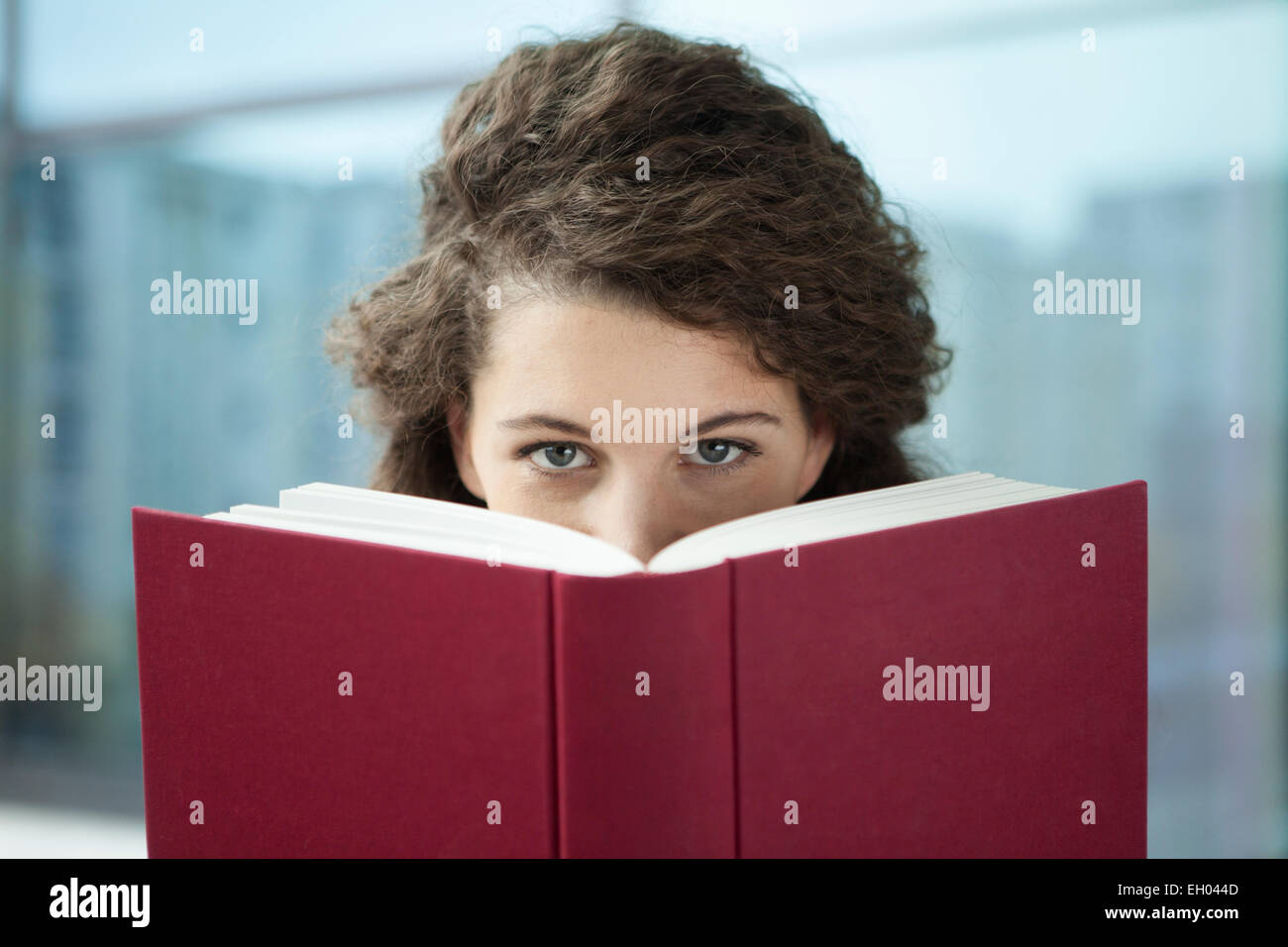 Young woman peeking from behind book Stock Photo
