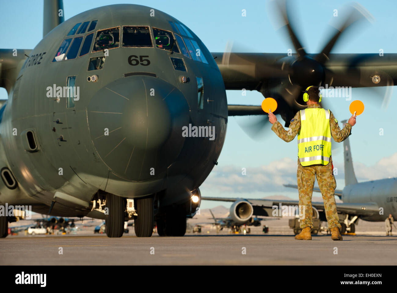 A Royal Australian air force aircraft maintainer marshals an RAAF C-130J Super Hercules into position after a training mission during Red Flag 15-1 at Nellis Air Force Base, Nev., Jan. 27, 2015. The mock battle training provided by Red Flag in the skies over the Nevada Test and Training Range has yielded results that increase the combat capability of U.S. and allied air forces for future real-world combat situations. Stock Photo