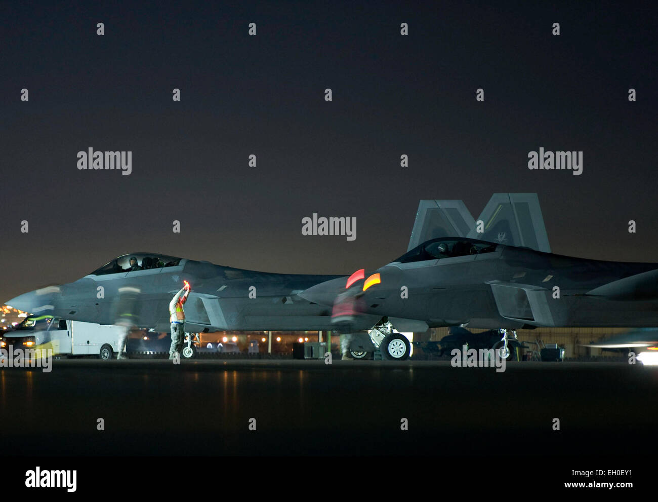 Two crew chiefs marshal F-22 Raptors assigned to the 94th Fighter Squadron at Joint Base Langley-Eustis, Va., at Nellis Air Force Base, Nev., Feb. 4, 2015. In addition to daytime operations, Red Flag conducts training exercises during the hours of darkness to train for low-visibility environments. Stock Photo