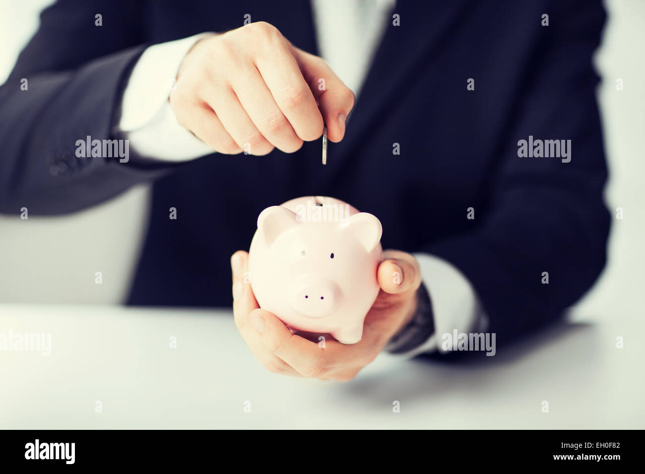man putting coin into small piggy bank Stock Photo - Alamy