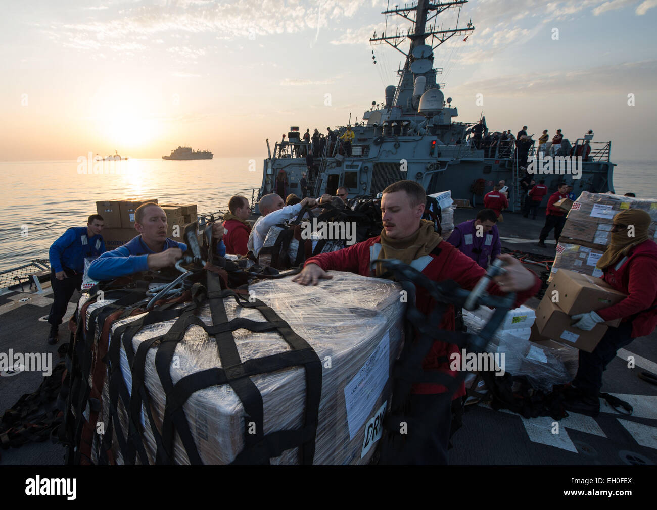 ARABIAN GULF (Feb. 13, 2015) Sailors aboard the guided-missile destroyer USS Mitscher (DDG 57) remove cargo nets from supplies after a vertical replenishment with the Military Sealift Command dry cargo and ammunition ship USNS Charles Drew (T-AKE 10) as an SA-330J Puma helicopter flies supplies to the USS Milius (DDG 69), background, left. Mitscher is deployed in the U.S. 5th Fleet area of operations supporting Operation Inherent Resolve, strike operations in Iraq and Syria as directed, maritime security operations and theater security cooperation efforts in the region. Stock Photo