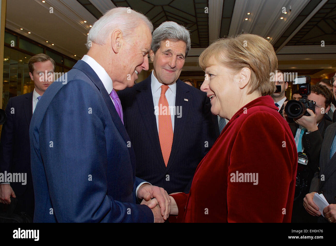U.S. Secretary of State John Kerry watches as Vice President Joe Biden greets German Chancellor Angela Merkel after she arrived at the Munich Security Conference in Munich, Germany, on February 7, 2015, to deliver a speech and meet with U.S., Ukrainian, and other government officials. Stock Photo