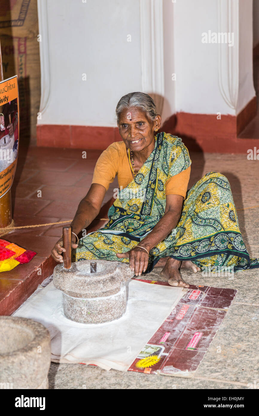 Old woman wearing a local style sari grinding rice flour by traditional methods at DakshinaChitra Heritage Museum, Chennai, Tamil Nadu, southern India Stock Photo