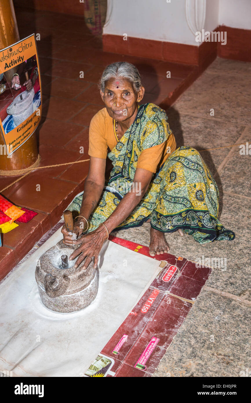 Old woman wearing a local style sari grinding rice flour by traditional methods at DakshinaChitra Heritage Museum, Chennai, Tamil Nadu, southern India Stock Photo