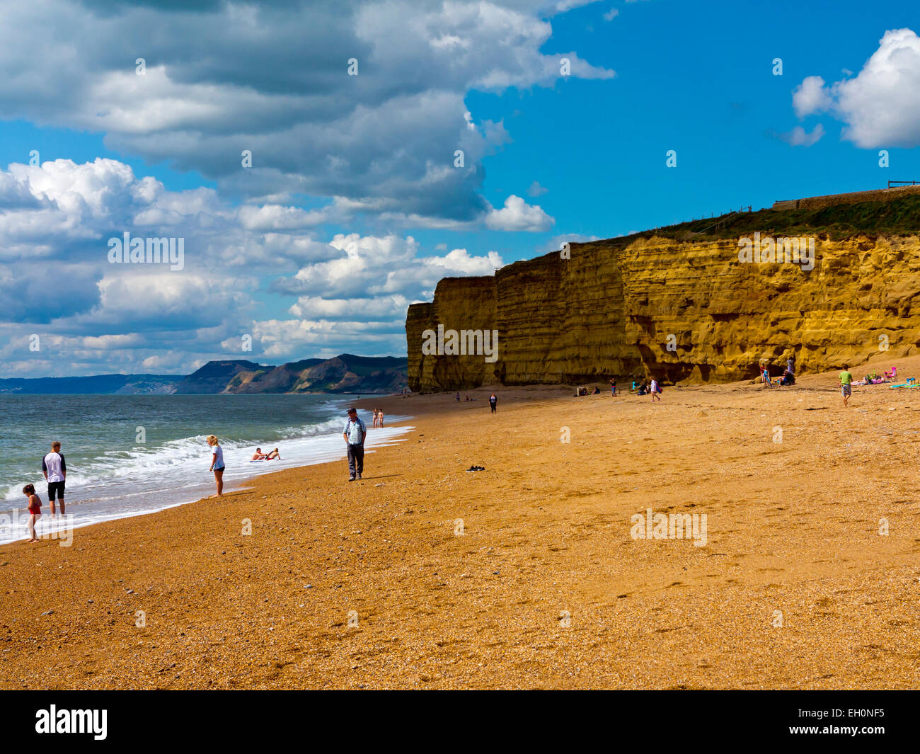 People playing on the beach with sandstone cliffs behind at Burton Bradstock on the Jurassic Coast south west England UK Stock Photo