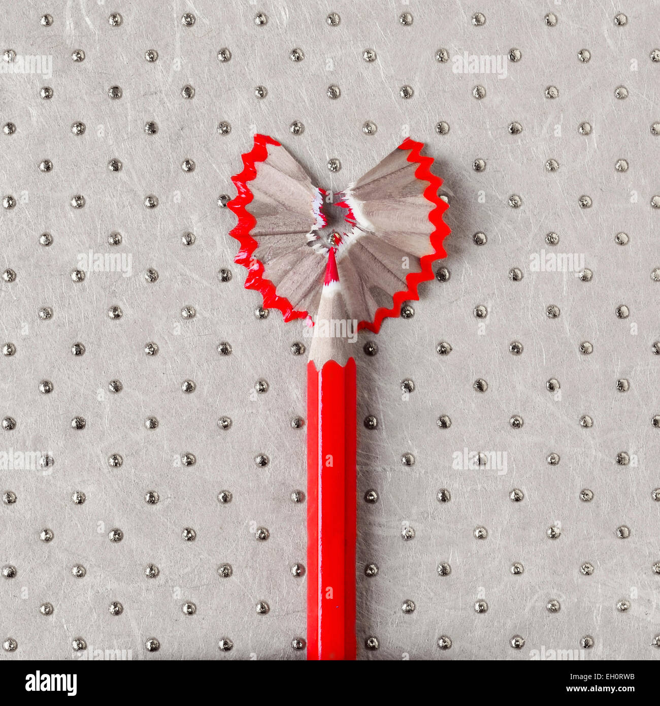 a sharpened wooden red coloured pencil with its shavings forming a heart on a patterned background Stock Photo