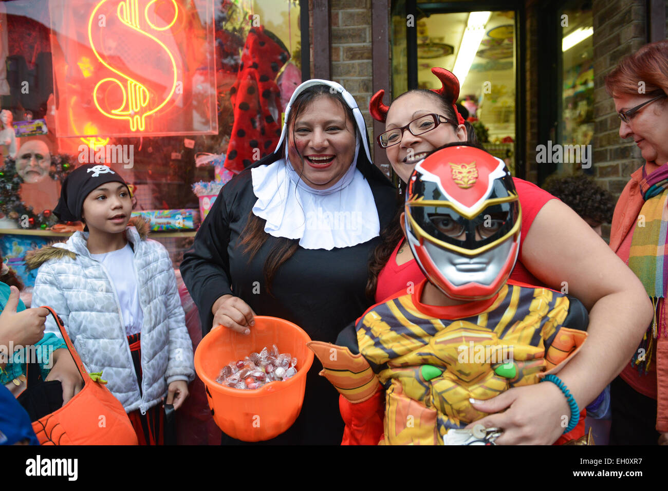 Woman dressed as a nun holding a bucket full of candy with people around her posing. Halloween 2013. Newark, New Jersey. Stock Photo