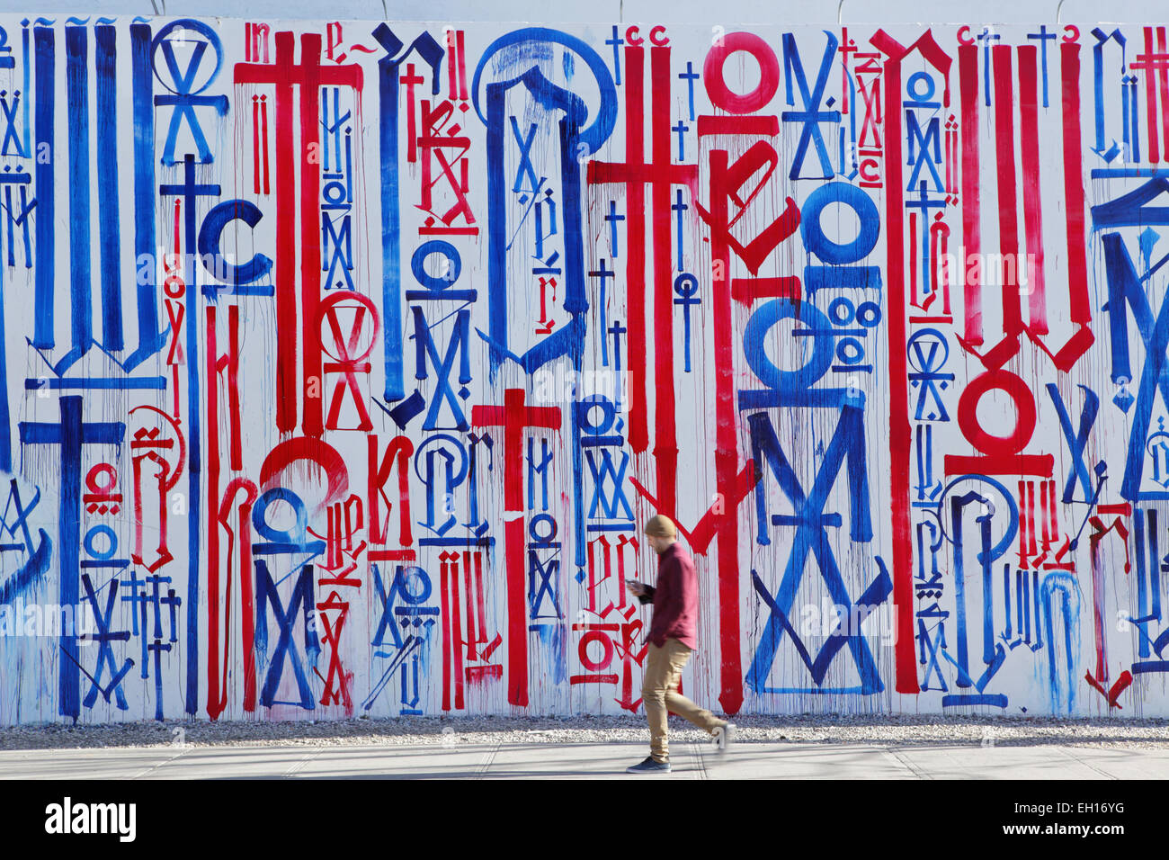Man walking to work past a colourful mural painted by RETNA on the Bowery Mural Wall on Houston Street, New York Stock Photo