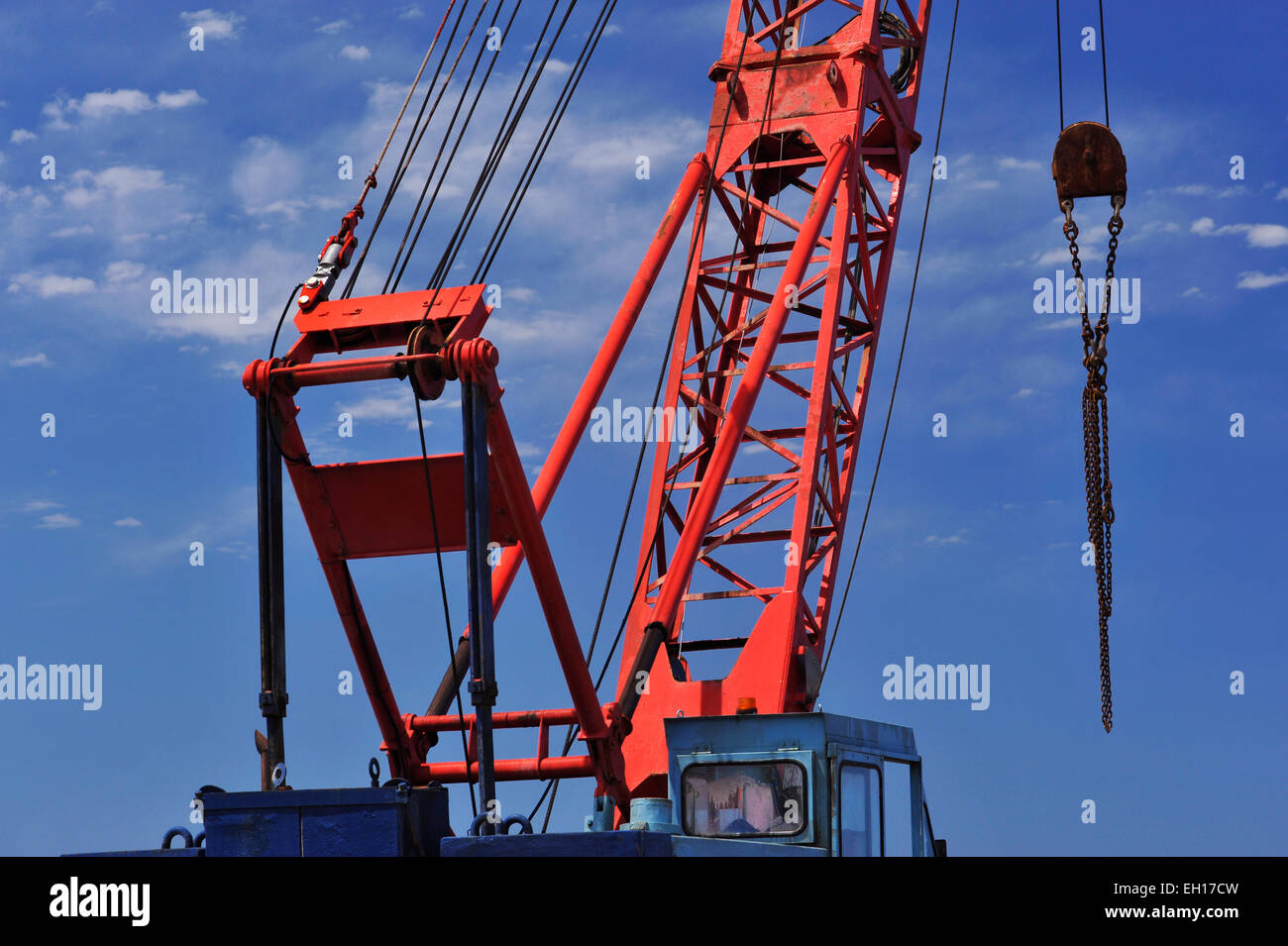Truss construction of red crane boom with cables and pulley chain is hanging at end of cargo hook Stock Photo
