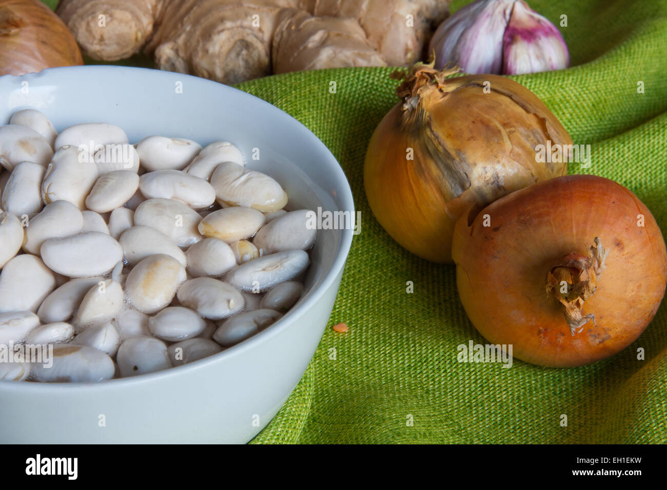 White beans getting soaked in water. Next  to it  raw onions and other vegetables Stock Photo