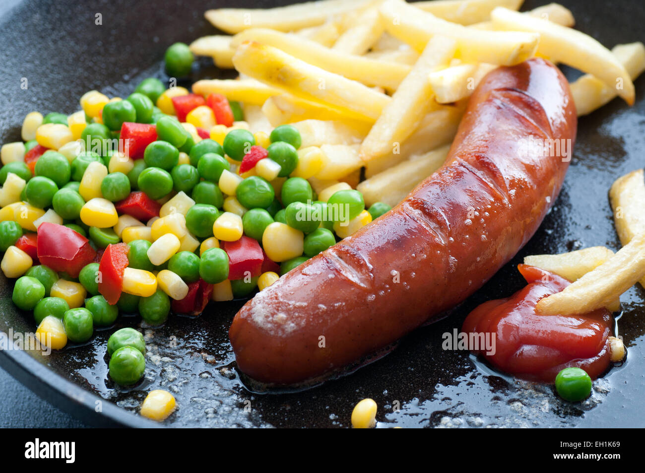 Sausage, french fries, vegetable mix and ketchup in a pan Stock Photo