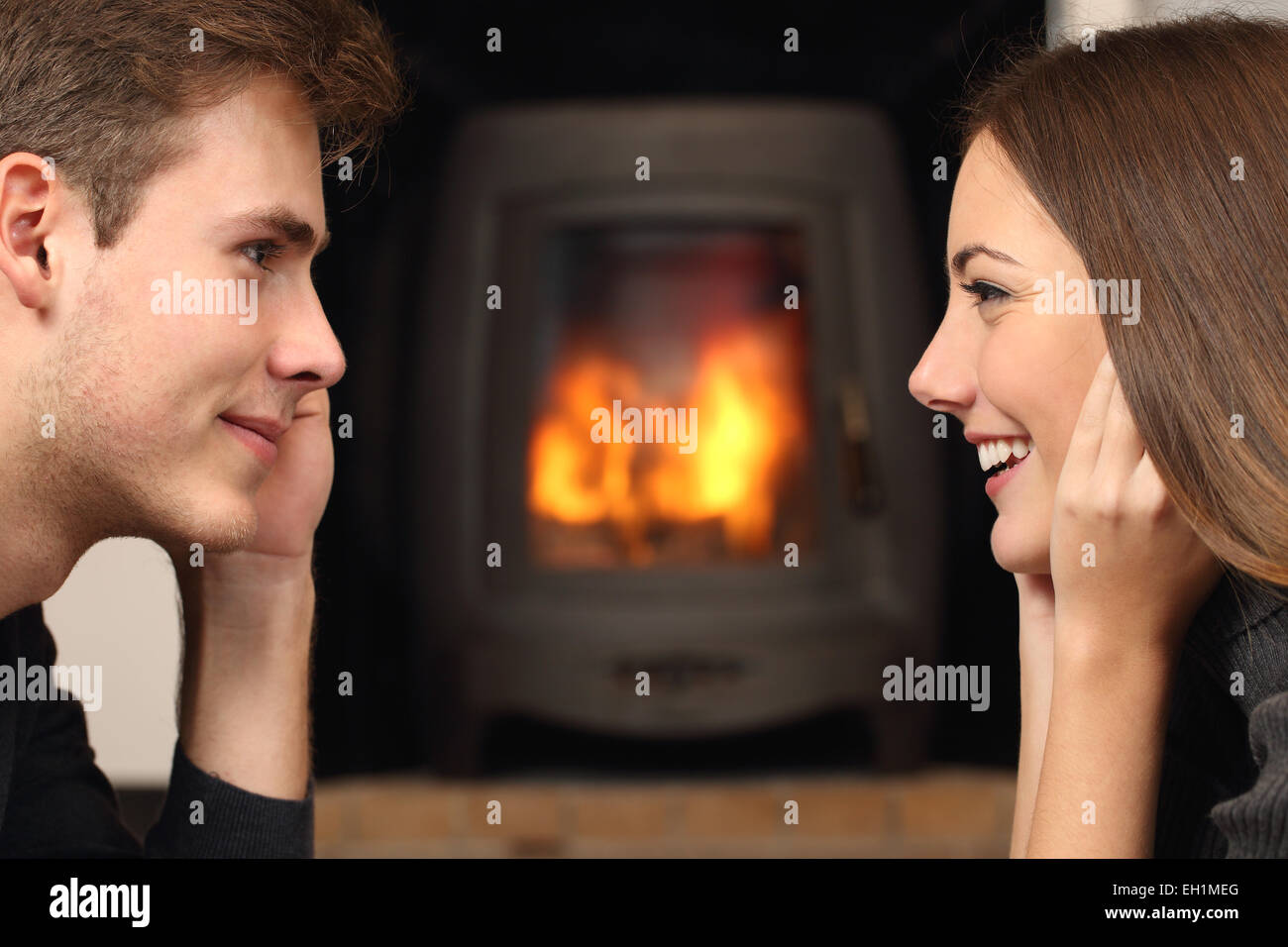 Side view of a couple flirting and looking each other in front a fireplace Stock Photo