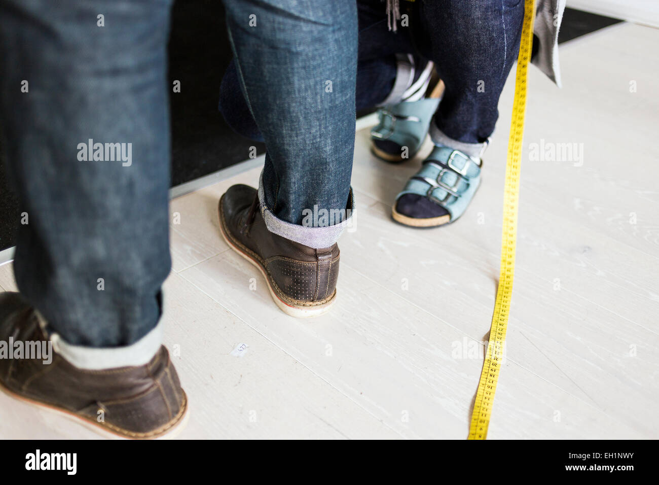 Low section of fashion designer measuring client's jeans with tape in