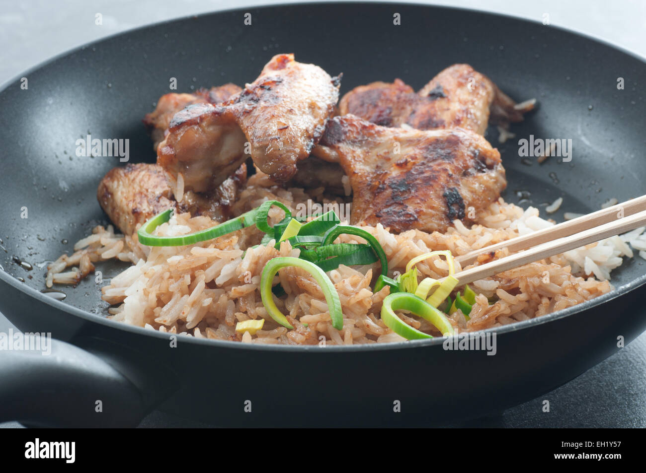 Leftovers. Fried rice with with soy sauce, barbecue chicken wings and leek in a frying pan. Stock Photo