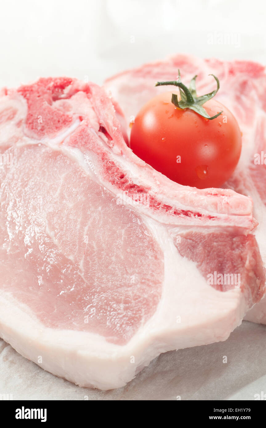 Raw mottled pork chops and a tomato on food paper. Stock Photo