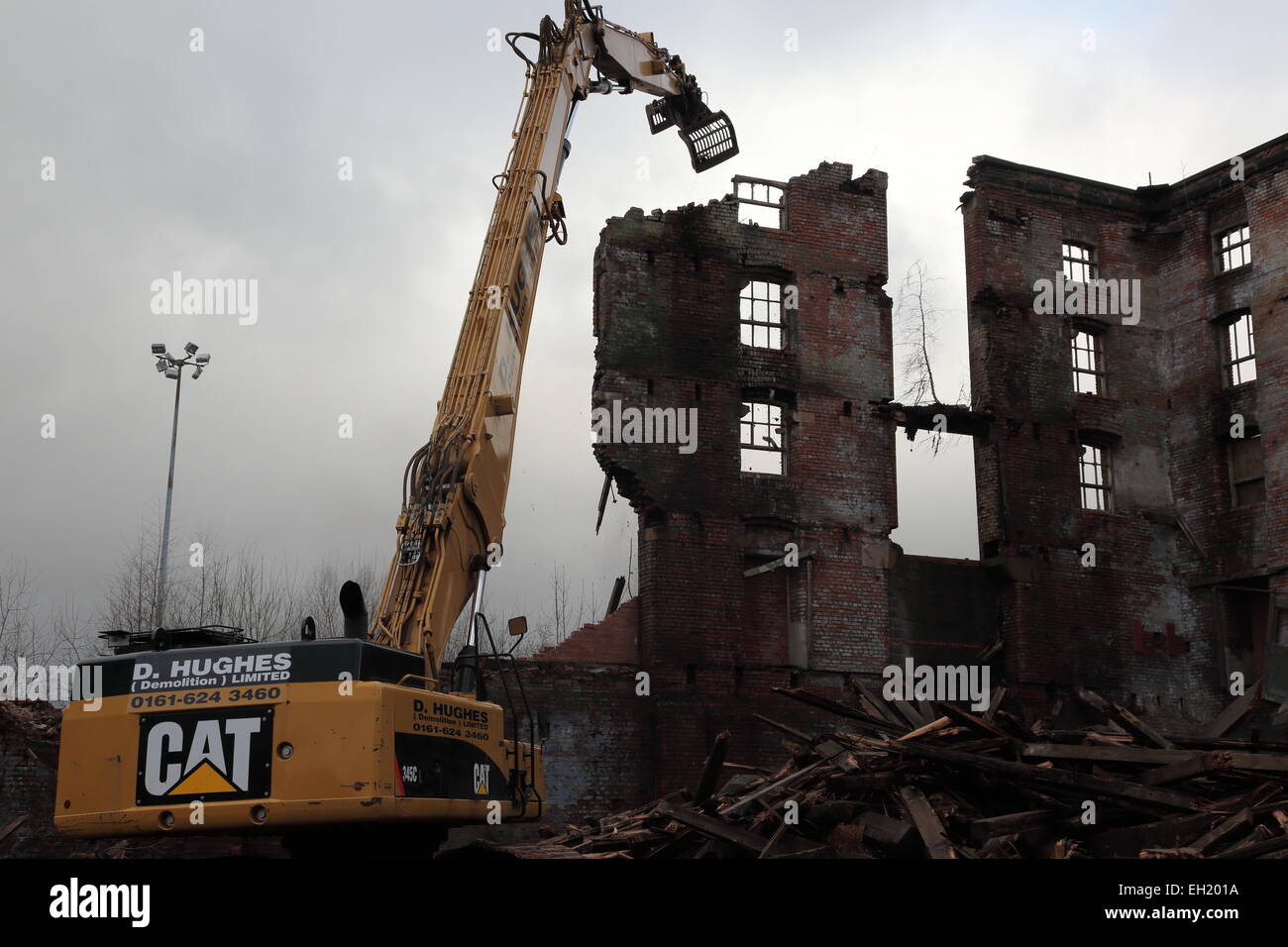 An old warehouse being demolished by a long reach excavator in Oldham, UK Stock Photo