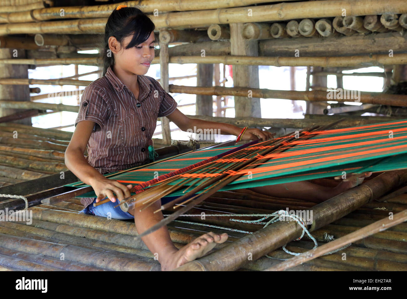 Girl sitting on the floor in a wooden house weaving on a narrow handloom. Kleronga village, Sumba island, Indonesia, Asia Stock Photo
