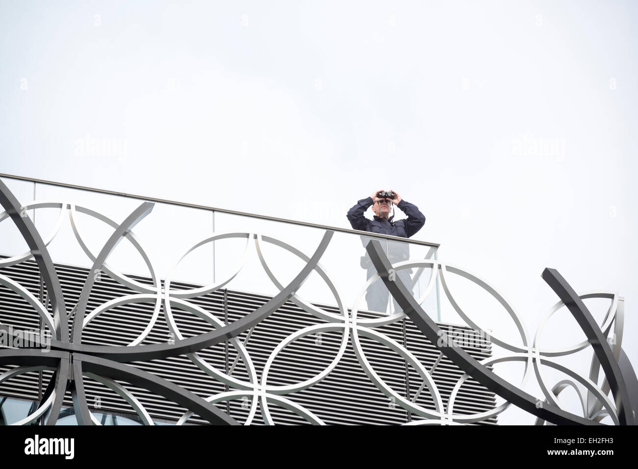 Police surveillance. Policeman looking through binoculars from balcony on Library of Birmingham at Conservative Party conference Stock Photo